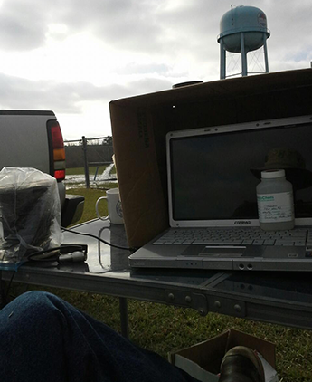OAI's Portable Field Office Next to Well #2's Test/Observation Well; Production Well's Discharge to Left of Laptop Screen